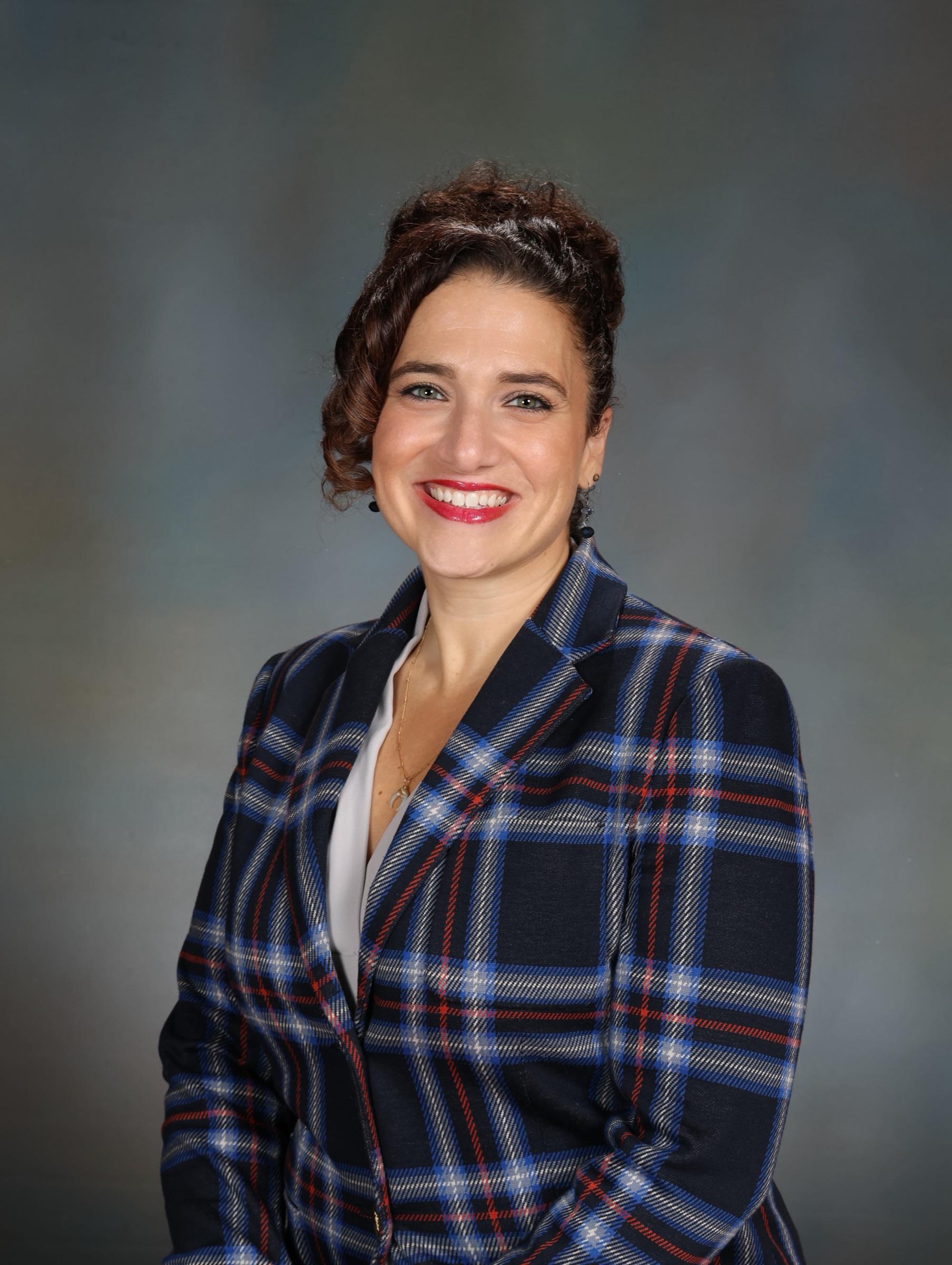 Nicole Stephenson, IOM — studio portrait in a navy and red plaid blazer.