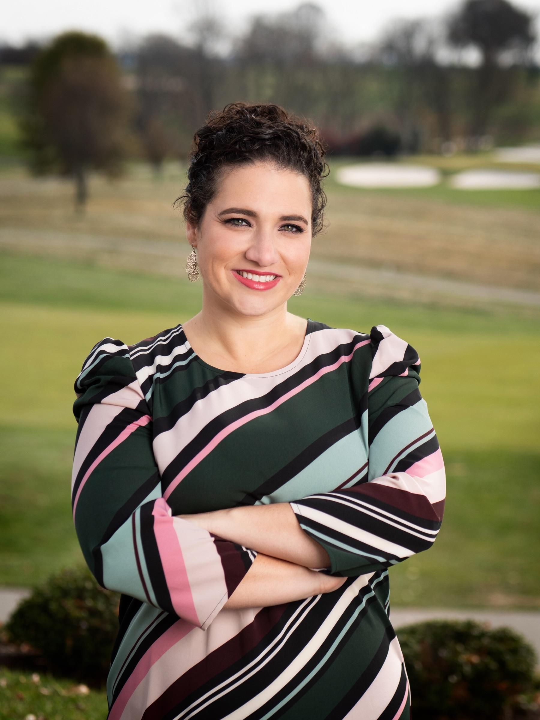 Nicole Stephenson — outdoor portrait in a striped dress with a rolling lawn behind her.
