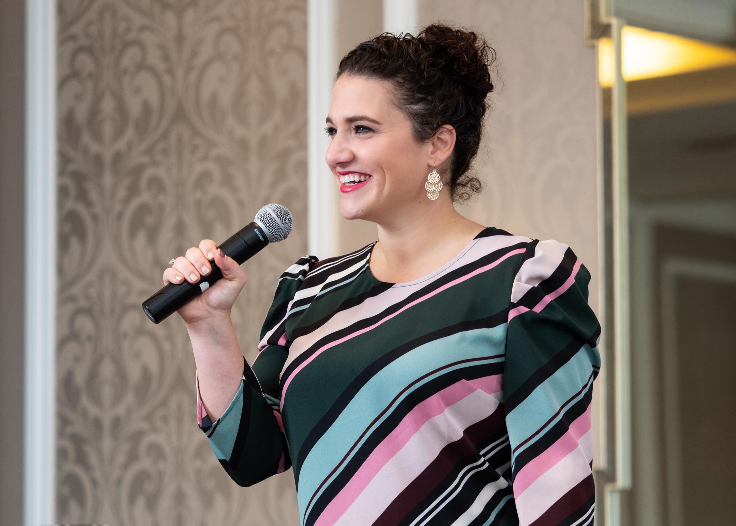 Nicole Stephenson on stage with a microphone, mid-keynote.