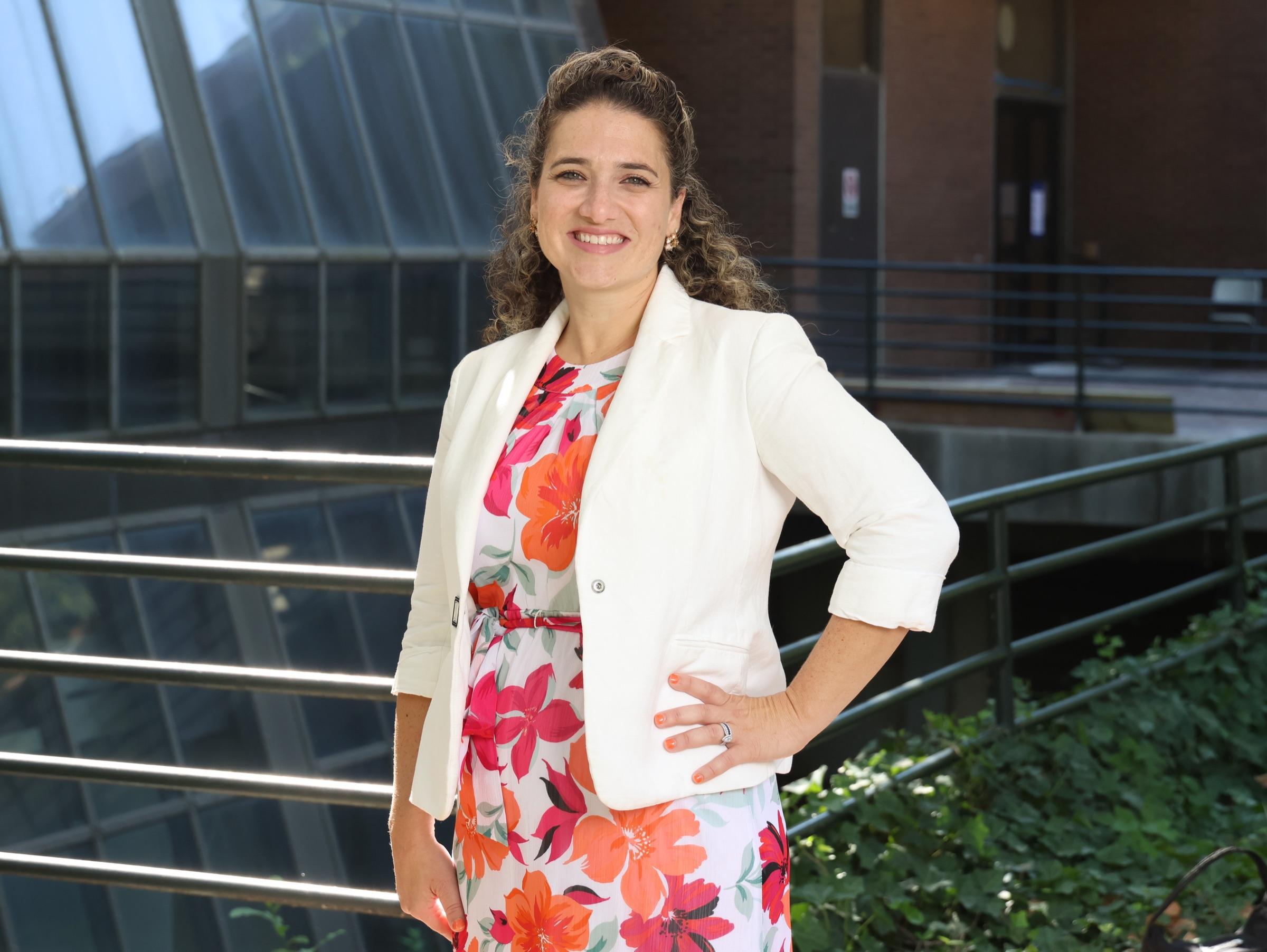 Nicole Stephenson on the University of Pennsylvania campus in front of the Wharton glass facade, in a floral dress and white blazer.